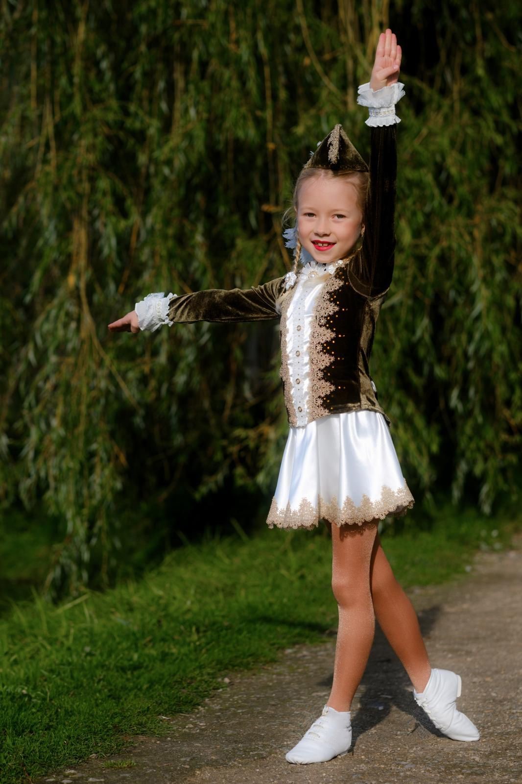Ein junges Gardemädchen posiert mit erhobenem Arm im braunen Kostüm im Freien vor einem Baum mit herbstlichem Laub.